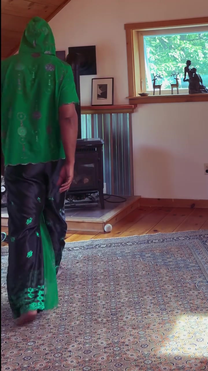 Back view of Kristopher wearing a green handmade hooded garment and patterned trousers.