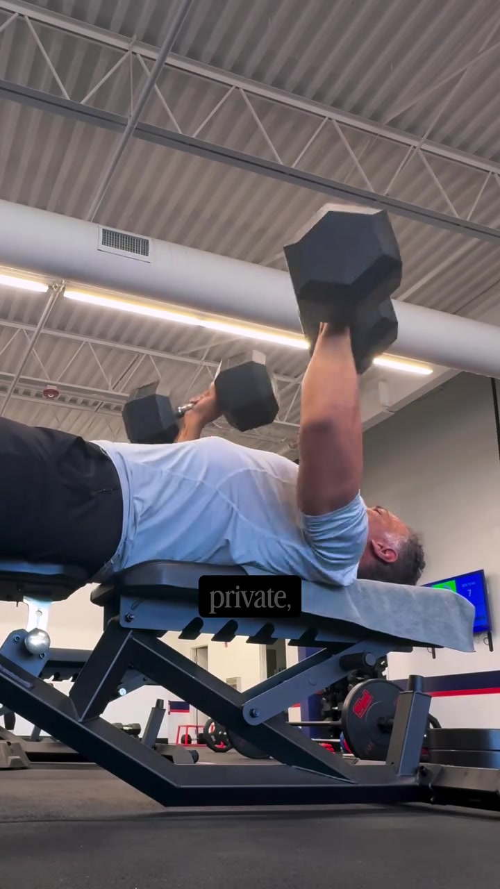 Kristopher performing a dumbbell press on a bench in an F45 studio.