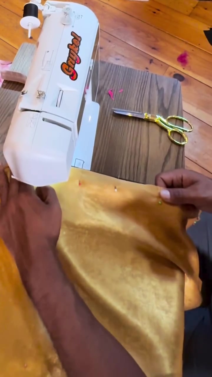 Kristopher stitching gold fabric at a sewing machine.